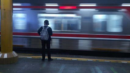 A lone commuter with a backpack stands on a station platform as a commuter train rushes past with dynamic motion blur. © Pandu