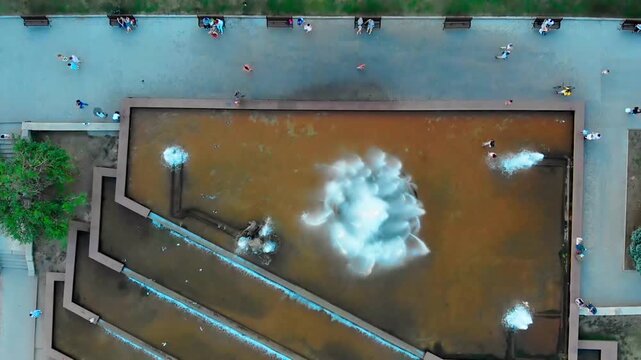 Aerial drone view of the famous Sadko Fountain in the center of Sumy, Ukraine during a hot summer day. People relax around the fountain, children play near the water