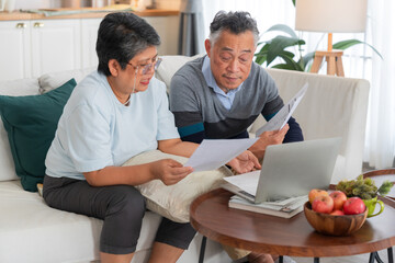 Senior Asian couple reviewing financial documents and bills with laptop computer at home concept for retirement planning savings account budget debt tax form insurance expenses © whyframeshot
