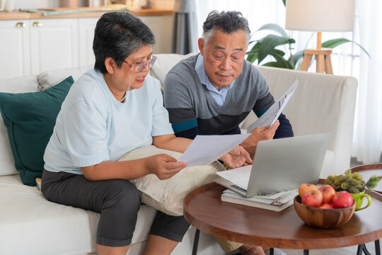 Senior Asian couple reviewing financial documents and bills with laptop computer at home concept for retirement planning savings account budget debt tax form insurance expenses