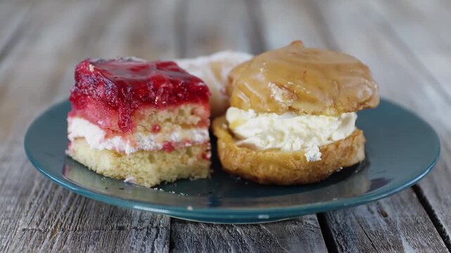 Man hand cutting raspberry jelly cake on plate with fork. Cream puff, cream roll in background. Sweet desert food clip