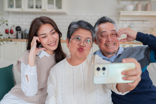 Happy Asian family taking a selfie with smart phone inside home kitchen concept for social media photo digital influencer technology marketing lifestyle happiness