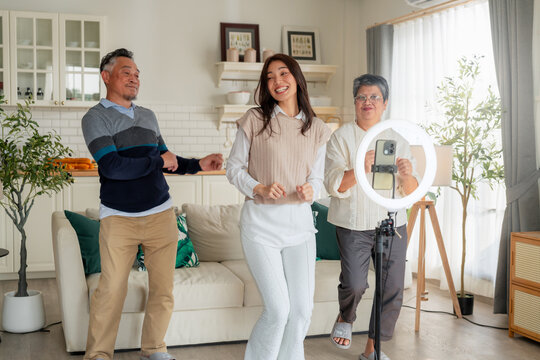 Active Asian multi-generation family dancing together for short video content online with smart phone and ring light inside home living room concept for social media challenge influencer 