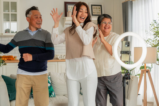 Happy Asian multi-generation family making vlog video live streaming online with smart phone and ring light inside home kitchen concept for social media influencer digital content creator technology m