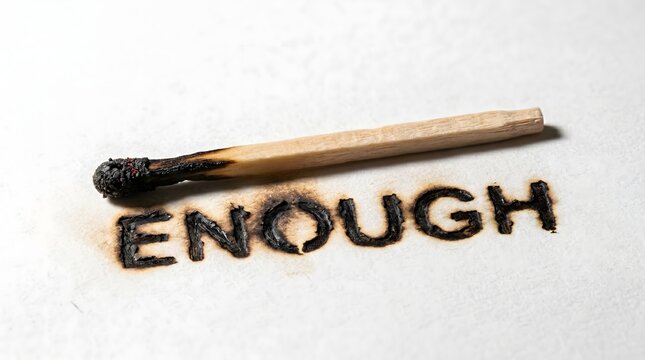 A burnt matchstick rests above the word 'ENOUGH' singed into white paper, symbolizing the physical and emotional exhaustion of burnout and reaching one's breaking point.
