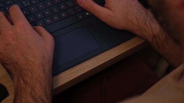 Close Up of Man Typing on Laptop Keyboard at Home Workspace. Detailed view of hands using a computer in a home office environment.