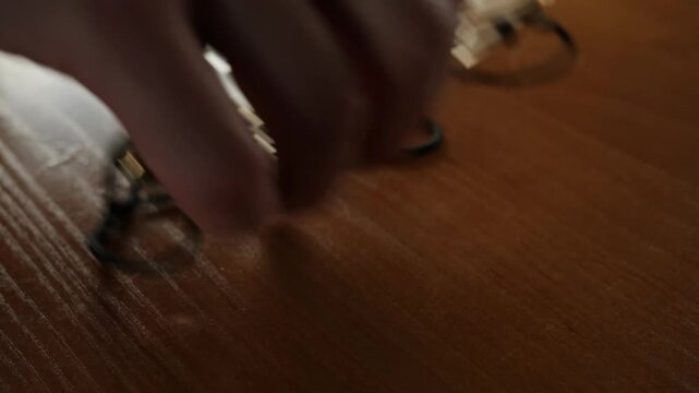 Hand reaching for eyeglasses with a black cord on a desk surface