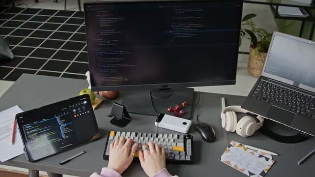 Medium top view of hands of unrecognizable female programmer writing algorithm with help from AI vibe coding agent, typing prompts and checking iterations, while developing mobile app in office