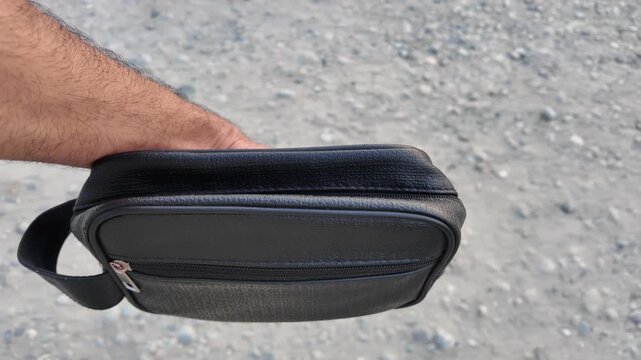 Black PU leather men&rsquo;s clutch with wristlet strap and zippered pocket outdoors in nature.