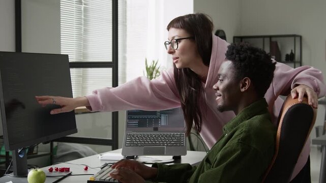 Medium side shot of young African American male programmer demonstrating new vibe coding agent to excited Caucasian female colleague, typing prompt, getting script prototype for improved productivity