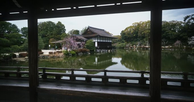 View of still pond, old Japanese building and spring cherry blossoms through wooden structure