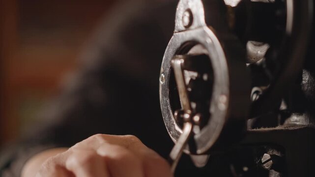 Close up of hand turning old sewing machine wheel under warm light. Detailed view of hand slowly rotating antique sewing machine wheel while lubricating gears in warm workshop setting