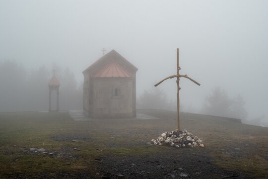 Misty hill holds quiet chapel and weathered cross. Holy Trinity Church in Gergeti