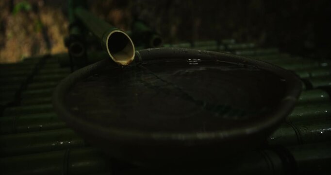 Water running through bamboo and into large bowl of water - closeup