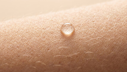 Fototapeta premium Macro close-up of a clear water droplet on hydrated human skin with detailed texture.