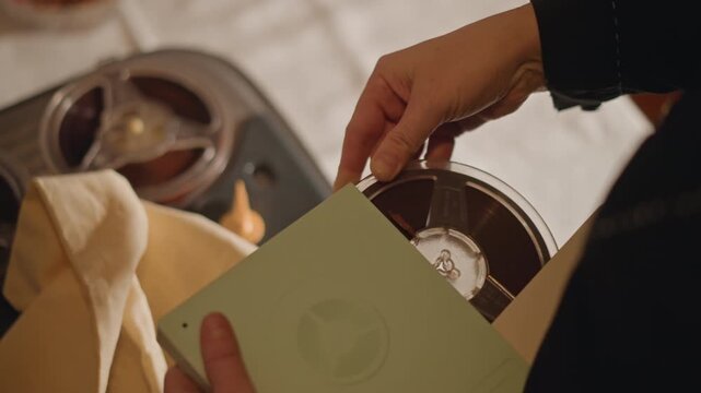 Gentle extraction of reel from storage canister. Systematic process of safeguarding old movie film reel. Meticulous procedure of removing and preserving archival film in protective containers