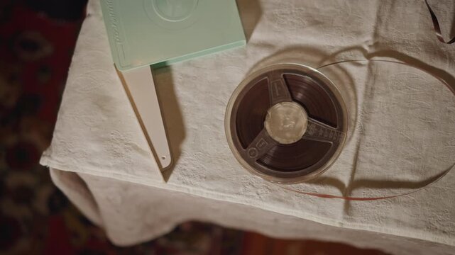 Vintage film reel on towel, mint green canister beside spool, warm lamplight and textured cloth, closeup of celluloid leader and grain, archival restorer prepping reel for inspection and scanning