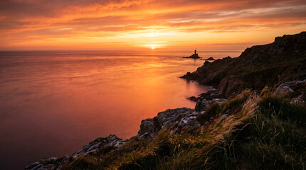 Obraz premium Puesta de sol desde un acantilado costero sobre un mar en calma en verano, con el agua pintada de naranja y rojo y larga exposición suavizando las olas.