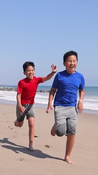 Two brothers playing tag on the beach in Santa Monica. Slow Motion. Vertical video.