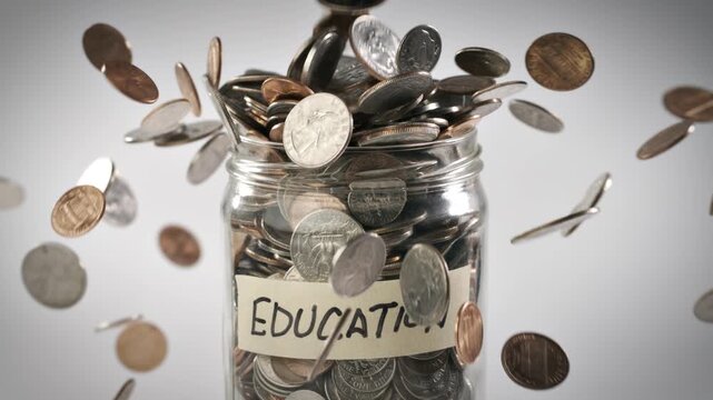 Close-up shot of coins falling in slow motion into a coin jar labeled 'Education'.