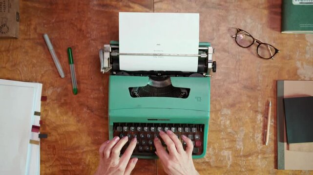 Overhead view of Brazilian hands typing on retro typewriter at wooden desk