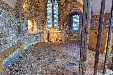 Fototapeta premium A stone room with a small wooden altar, large arched windows, and a patterned brick floor at Gloucester Cathedral - Gloucester - Gloucestershire - UK