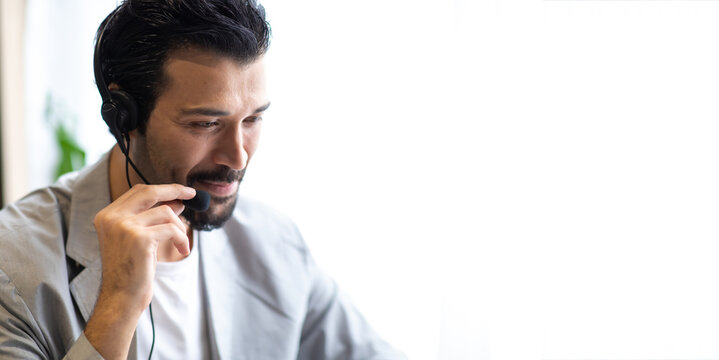 Attractive business man in suits and headsets smiling while working on desktop computer at modern office desk . Customer service assistant working in office. VOIP Helpdesk headset