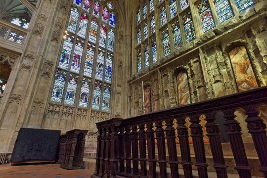 An interior view of a historic cathedral featuring prominent, vibrant stained-glass windows and intricately carved stone walls at Gloucester Cathedral - Gloucester - Gloucestershire - UK
