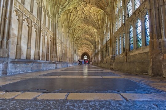 A long, grand stone corridor features an ornate vaulted ceiling and arched windows at Gloucester Cathedral - Gloucester - Gloucestershire - UK