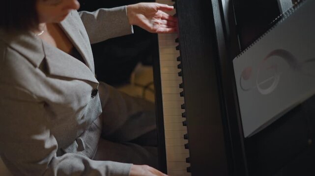Overhead white pianist mentor preparing at keyboard, blazerclad instructor checking score and posture, quiet rehearsal with thoughtful expression and soft interior lighting, professional teaching