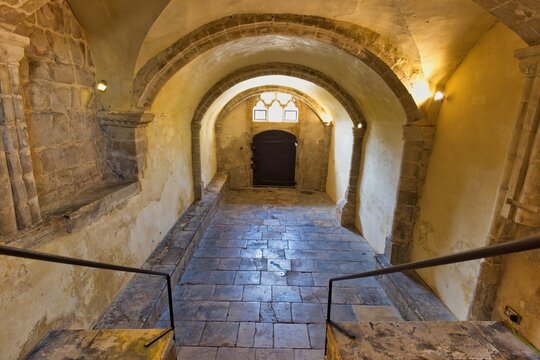 A stone archway leads down steps into a vaulted passage. This ancient structure features stone walls, a tiled floor at Gloucester Cathedral - Gloucester - Gloucestershire - UK