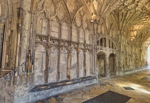 A historic stone cloister features detailed Gothic archways and intricate ribbed vaulting stretching into the distance at Gloucester Cathedral - Gloucester - Gloucestershire - UK