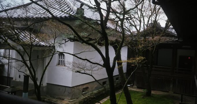 Little boy in Japanese structure staring out at old buildings and trees - panning shot