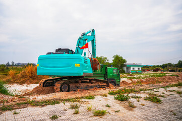 Fototapeta premium Turquoise crawler excavator excavating at construction site on Phu Quoc Island in Vietnam. Green excavator digs at construction site. 