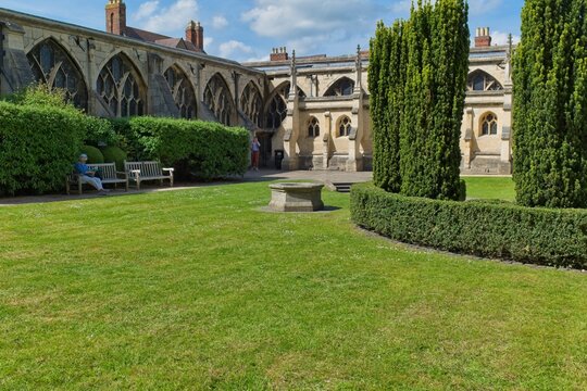 A sunny courtyard with a manicured green lawn, surrounded by historic stone buildings featuring arched windows at Gloucester Cathedral - Gloucester - Gloucestershire - UK