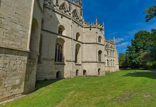 A historic light-stone building, possibly an abbey or cathedral, stands beside a lush green lawn under a clear blue sky at Gloucester Cathedral - Gloucester - Gloucestershire - UK