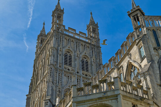 A historic stone cathedral with ornate towers and detailed architecture stands against a clear blue sky at Gloucester Cathedral - Gloucester - Gloucestershire - UK