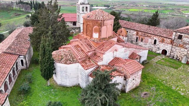 High-angle aerial shot descending over the ancient Byzantine brick domes, weathered red tile roofs, and courtyard of St. Mary Church at Apollonia Archaeological Park, Albania