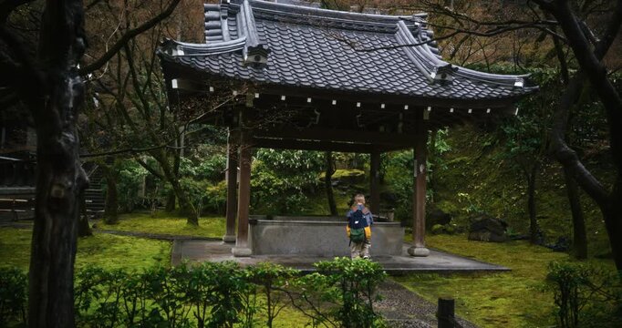 Little boy with backpack walking up to old Japanese structure in lush area - steady cam movement