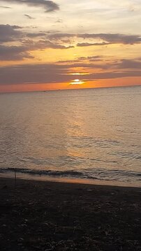 Beautiful golden sunset over a black sand beach with calm sea water and colorful evening sky. Peaceful coastal scenery with warm sunlight reflection, located at Singaraja, Bali, Indonesia.