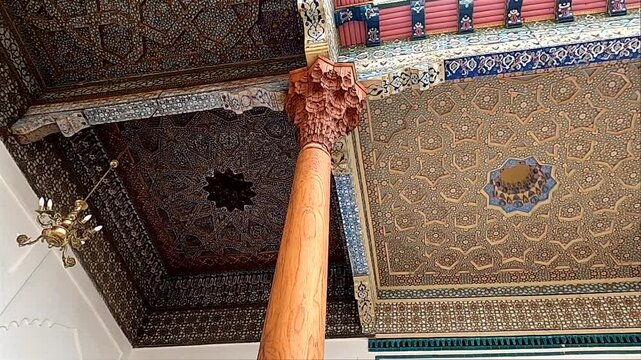 Carved wooden pillar and painted ceiling patterns at Bolo Hauz mosque