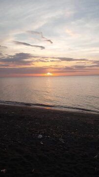 Beautiful golden sunset over a black sand beach with calm sea water and colorful evening sky. Peaceful coastal scenery with warm sunlight reflection, located at Singaraja, Bali, Indonesia.