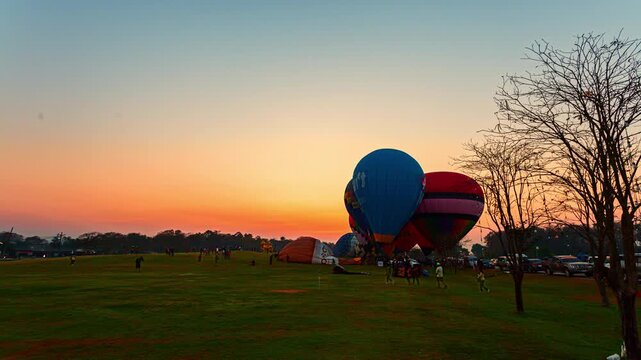 Chiang Rai,Thailand - February 18,2024: Time lapse view of numerous hot air balloons floating above the valleys as golden sunlight paints the horizon during a ballooning event in northern Thailand.