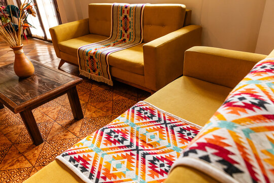Yellow sofa decorated with colorful indigenous handmade blanket in a cozy living room interior. Cozy home styling with traditional Andean textile runner on a modern couch.