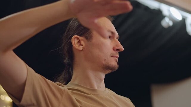 Male caucasian conductor leading rehearsal with expressive hand gestures and focused profile, intimate studio masterclass atmosphere, teaching technique to students, subtle stage lighting, casual