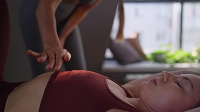 Woman exercises Glute bridge on a reformer bed machine with trainer in natural sunlight, focusing on pelvis and hips