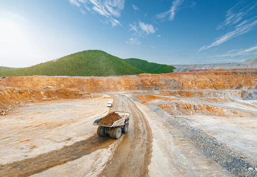 Aerial top view Mining dump truck transporting golden ore on curved haul road in open pit