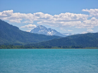 Obraz premium Germany, Scenic alpine beach landscape at Forggensee with snow covered mountain peaks and crystal waters