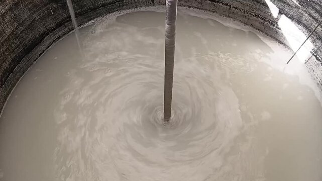 Industrial process of water treatment chemicals vigorously mixing with incoming filling water inside a large circular holding tank.