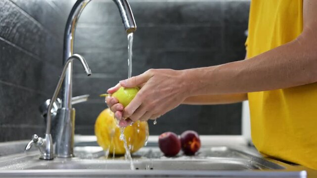 Washing ripe pear under running water in kitchen before eating video Full HD